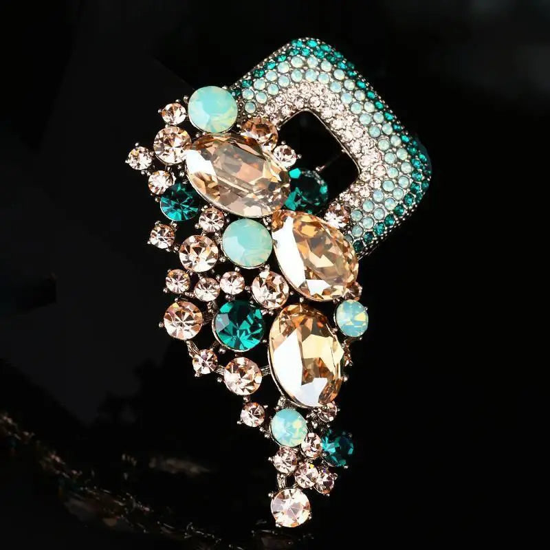 A crystal flower brooch pin for women featuring a sparkling teal and gold rhinestone design with a square base and cascading teardrop-shaped stones.