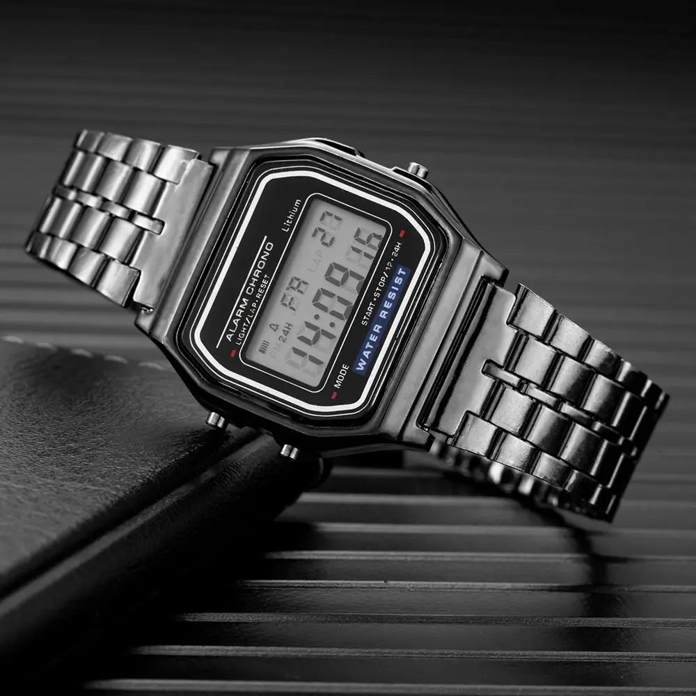 Des hommes ont conduit une montre numérique avec un écran LCD noir et un boîtier rectangulaire en acier inoxydable à tons argentés ainsi qu’un bracelet métallique, indiquant l’heure et la date.