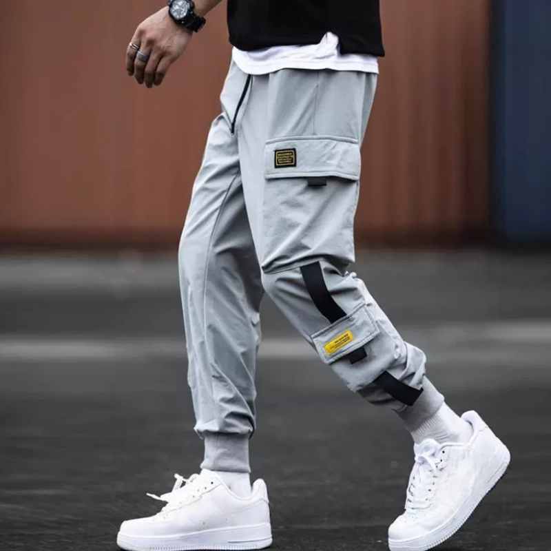 Pantalons cargo gris pour hommes avec plusieurs poches, accents noirs et jaunes, taille à cordon de serrage et coupe ample conçue pour un usage décontracté.