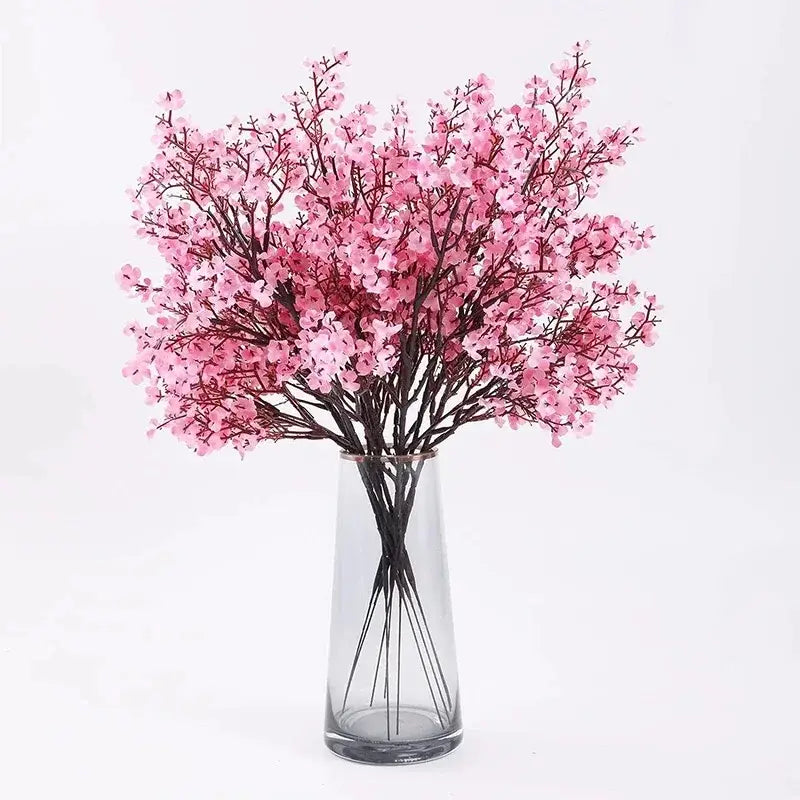 A delicate arrangement of artificial flowers cherry pink blossoms with dark stems displayed in a clear glass vase.