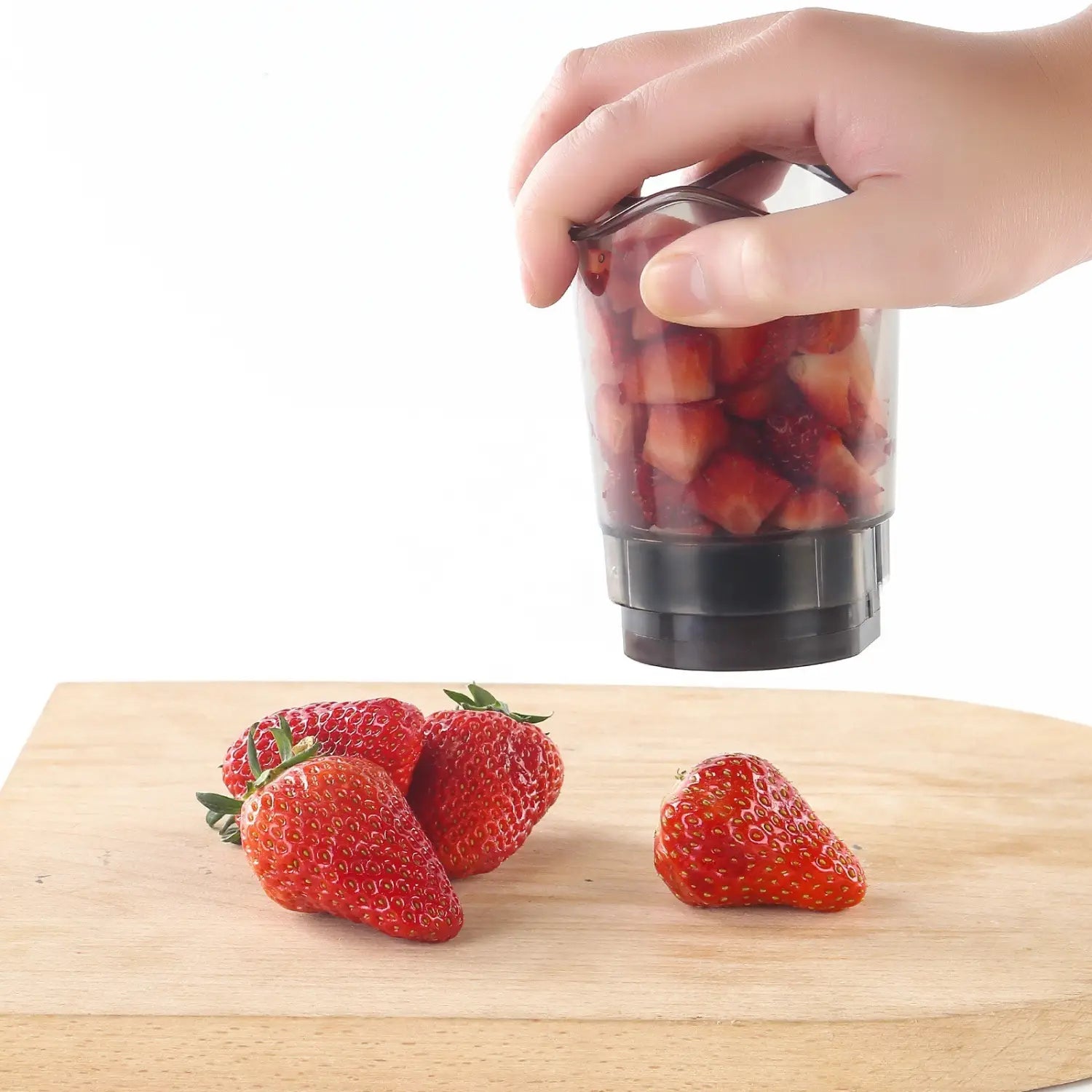 Transparent plastic handheld fruit and vegetable chopper slicer cup with black base filled with chopped red strawberries.