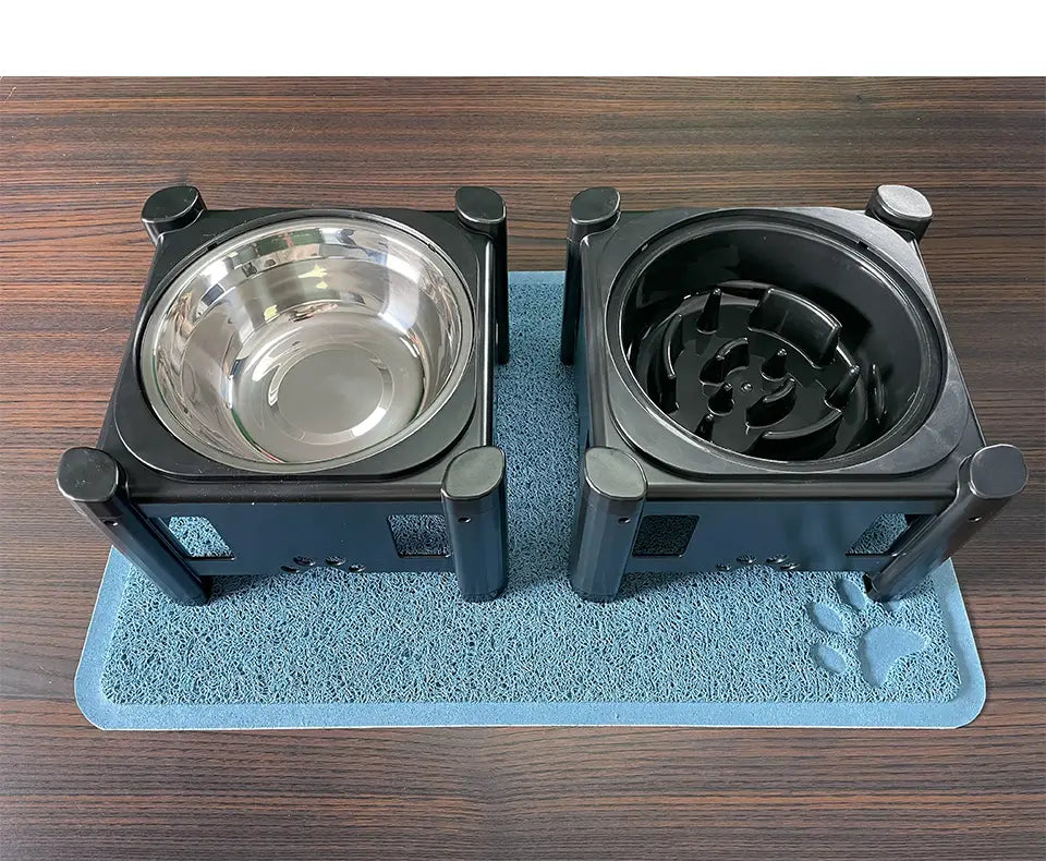 black waterproof dog feeding mat measuring 24 by 16 inches with a dual pet feeder featuring one stainless steel bowl and one maze puzzle bowl on a black stand placed over a blue paw-print feeding mat and litter mat