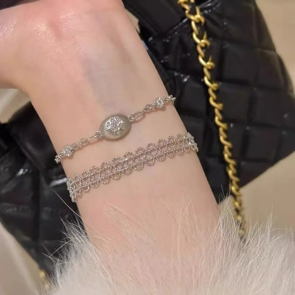 Silver metal lace bracelet with adjustable chain featuring a round diamond-encrusted pendant and delicate lace-like detailing.