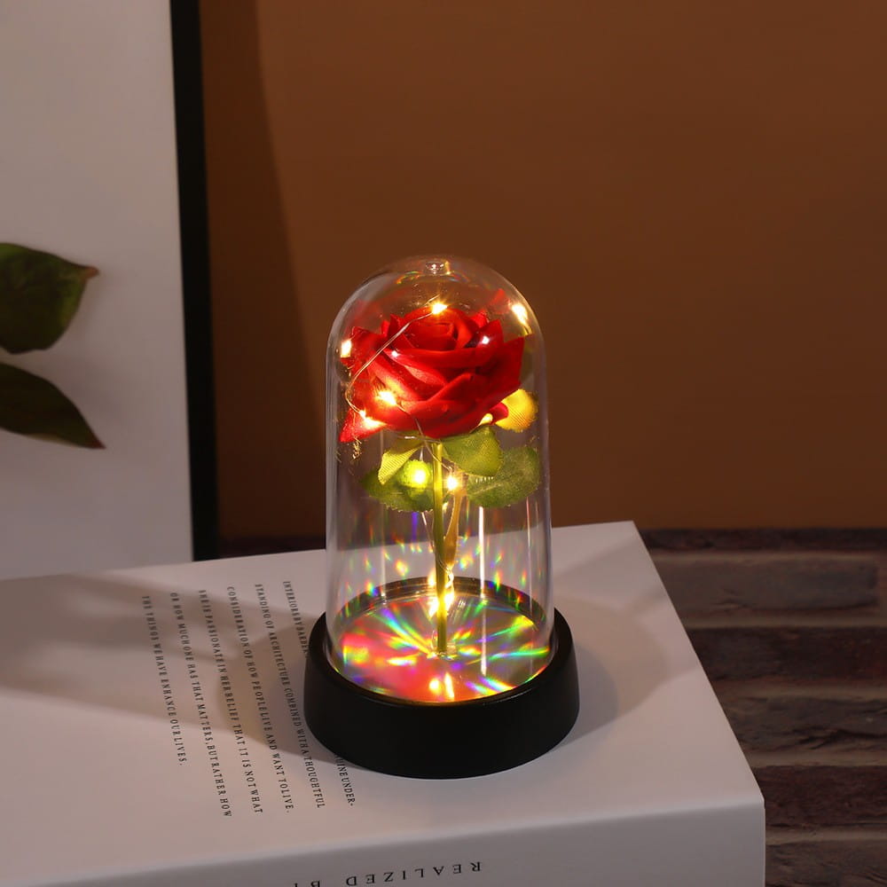 Une rose rouge luisante enfermée dans un dôme en verre transparent avec des lumières intégrées, reposant sur une base noire dans le cadeau de fleur lumineux en dôme de rose éternelle.