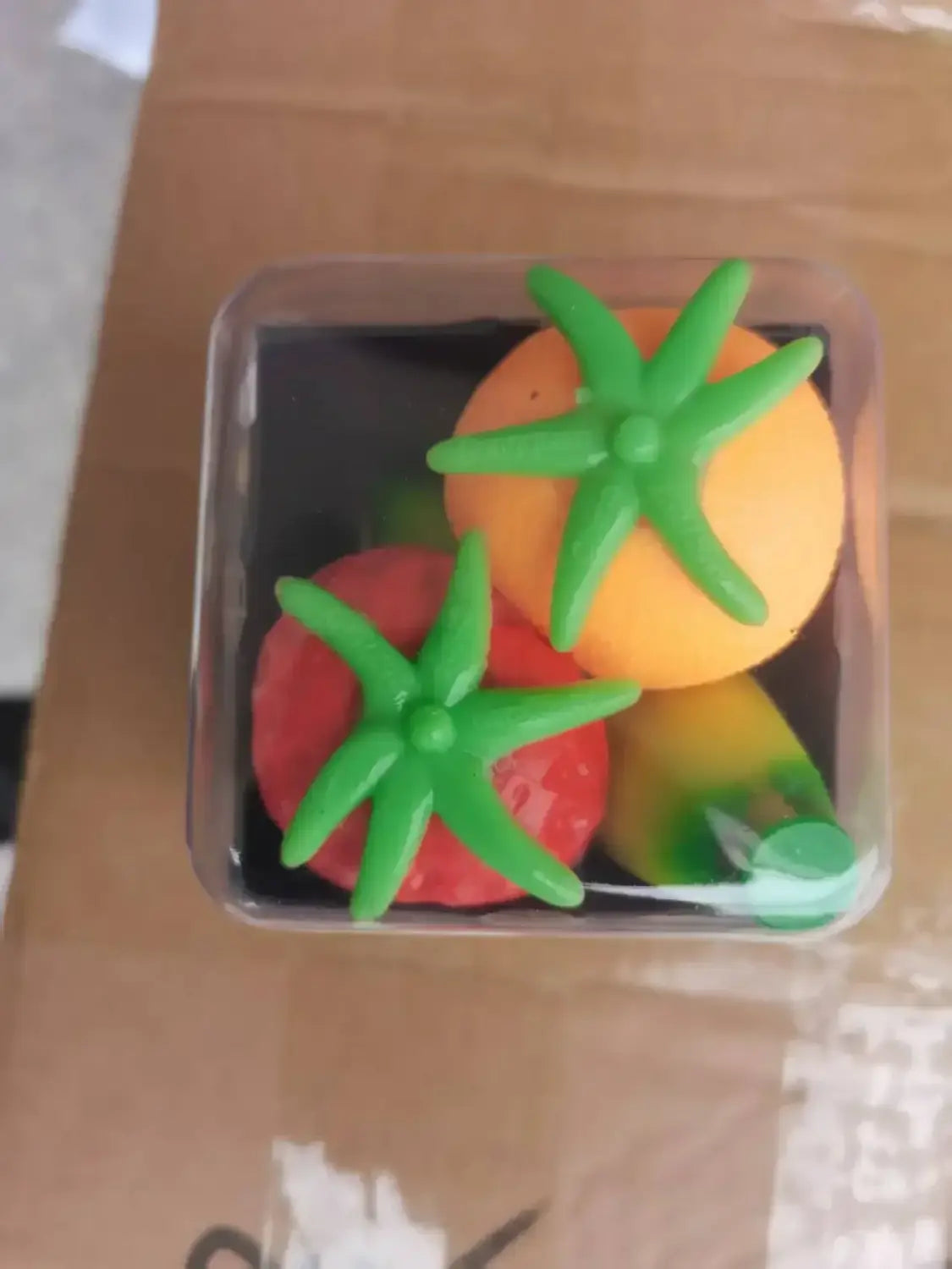 Ein transparenter Kunststoffbehälter zeigt farbenfrohe, sternförmige Erdbeere-Orange-Quetschspielzeuge aus weichem Silikon in einer Frontansicht.