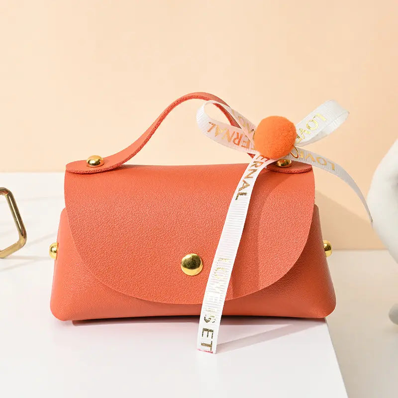 Mini sac à main en faux cuir de couleur corail avec quincaillerie ton or et un ruban blanc décoratif noué en forme de nœud, avec un pompon orange, conçu comme sac cadeau de mariage en cuir.