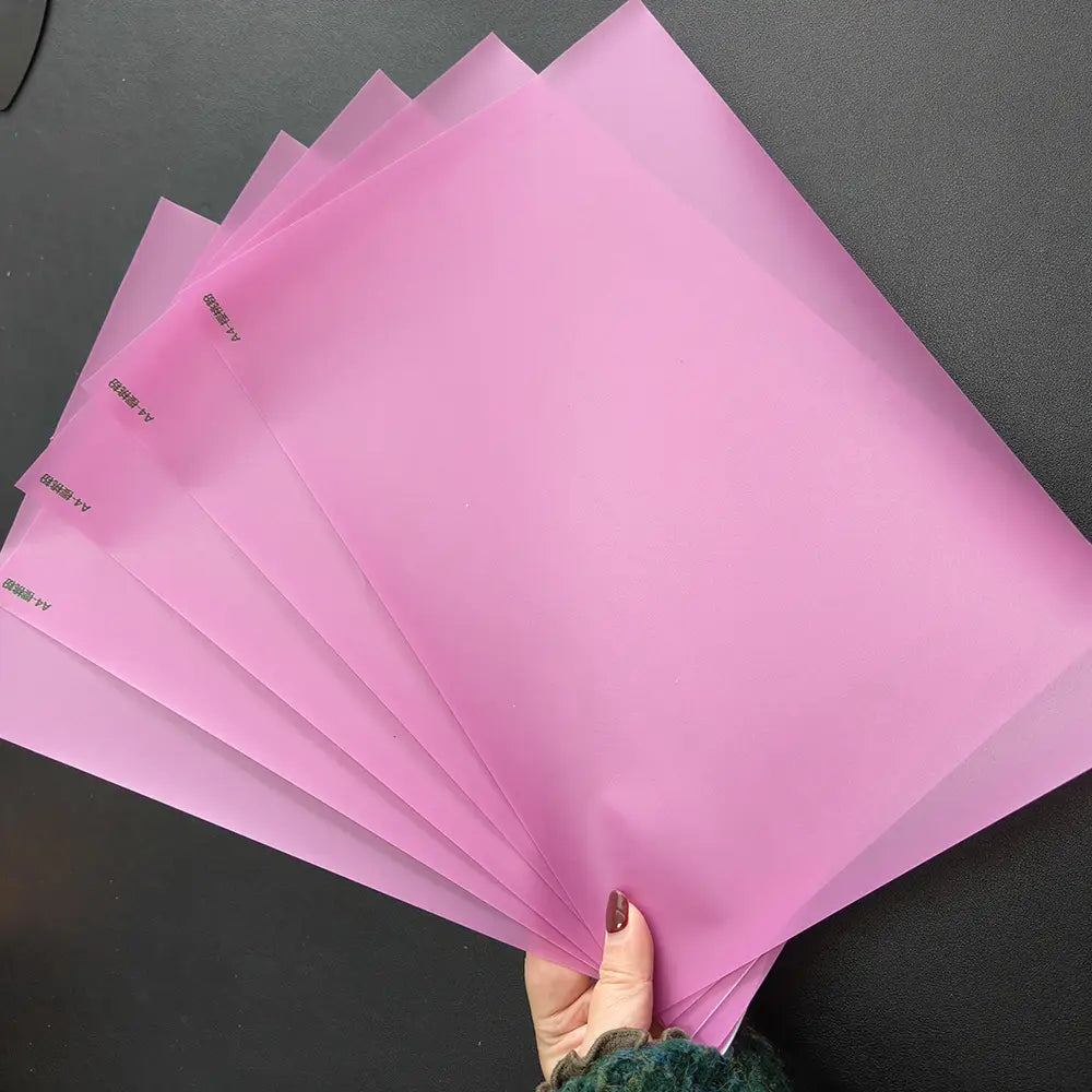 Carpetas de archivo de plástico rosa translúcidas mostradas junto con una máquina de laminación al vacío de película para teléfonos móviles, destacando la eficiencia del costo de envío y la aplicación del teléfono móvil.