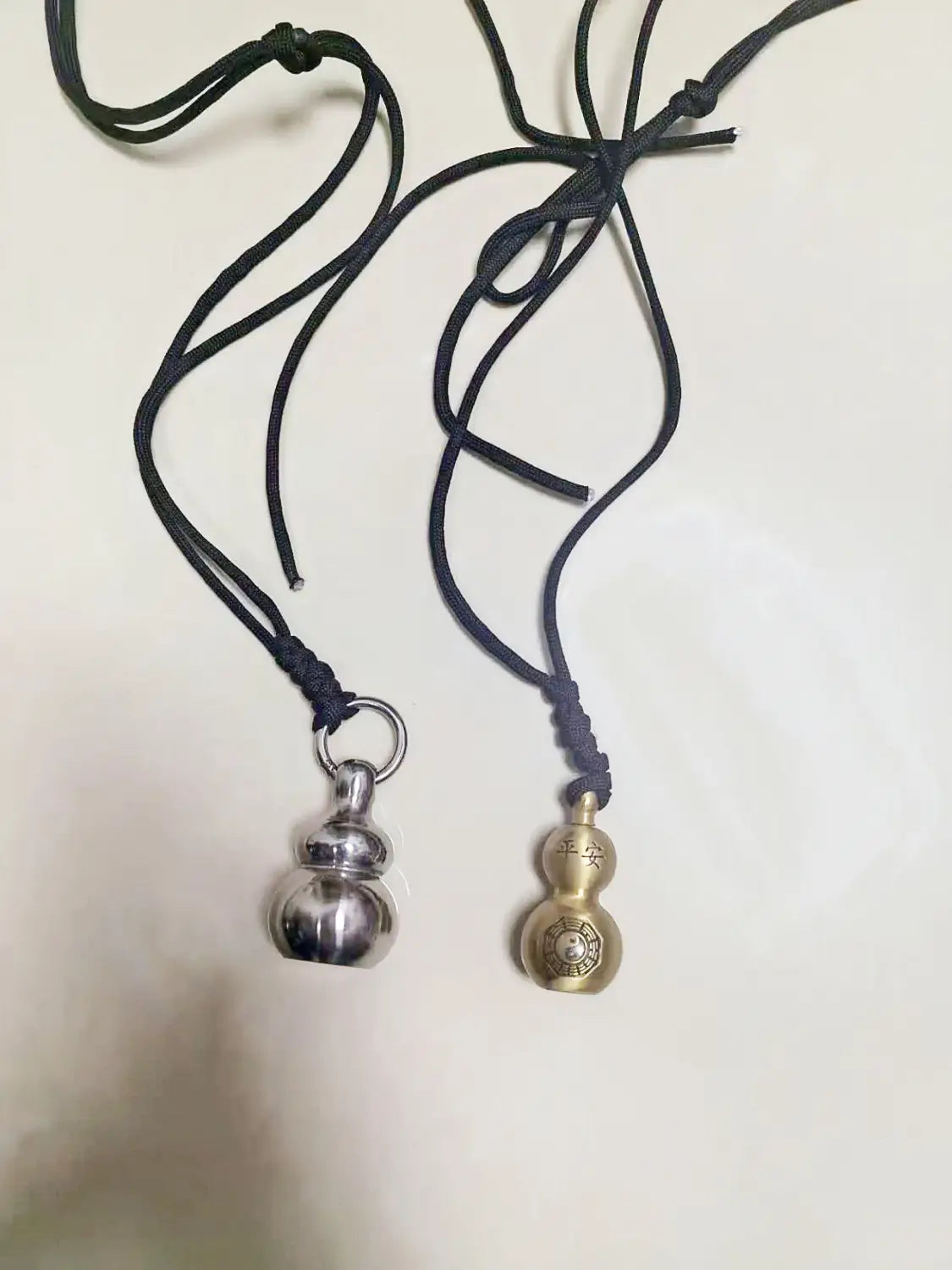 two black corded necklaces each featuring a metallic gourd-shaped pendant one polished silver and the other brass with engraved chinese characters designed as brass gourd self defense pendant necklaces