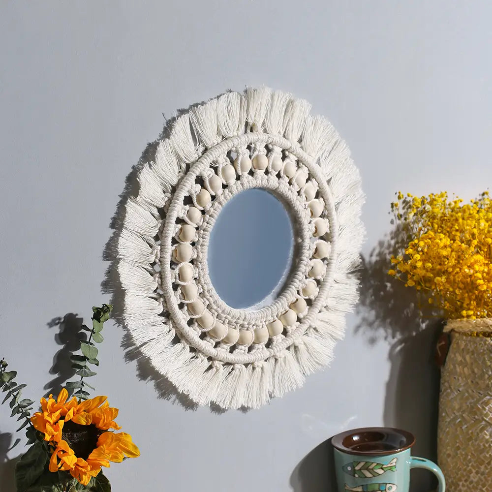 A white macrame-framed round mirror with tassels and beaded details designed as a boho decorative wall mirror.