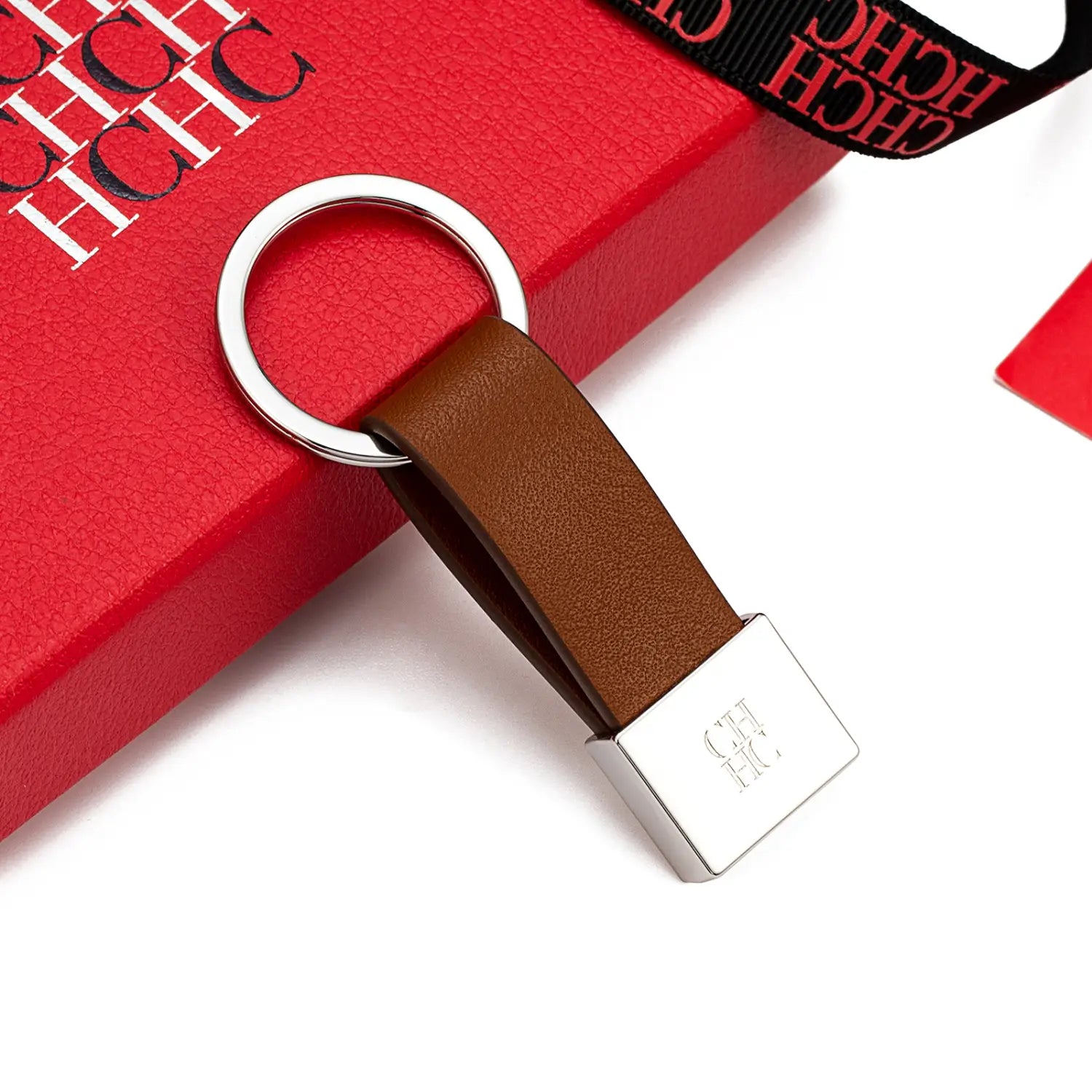 Porta llaves de cuero marrón con un anillo metálico plateado y una placa rectangular grabada con el logotipo ch, diseñado como accesorio de equipaje minimalista.