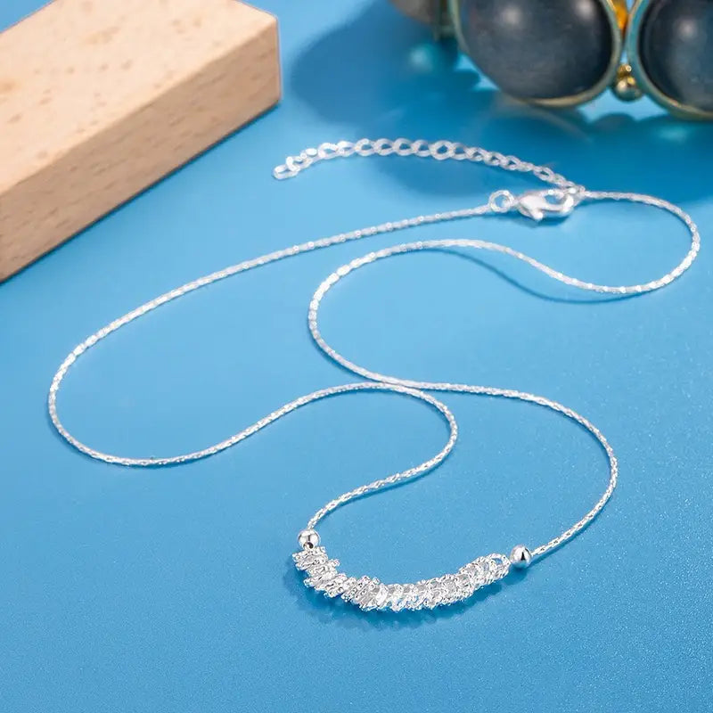 Collar minimalista de cadena tipo eslabones de papel en plata de ley, que presenta una cadena delicadamente texturizada y un colgante central tipo barra adornado con cristales que brillan.