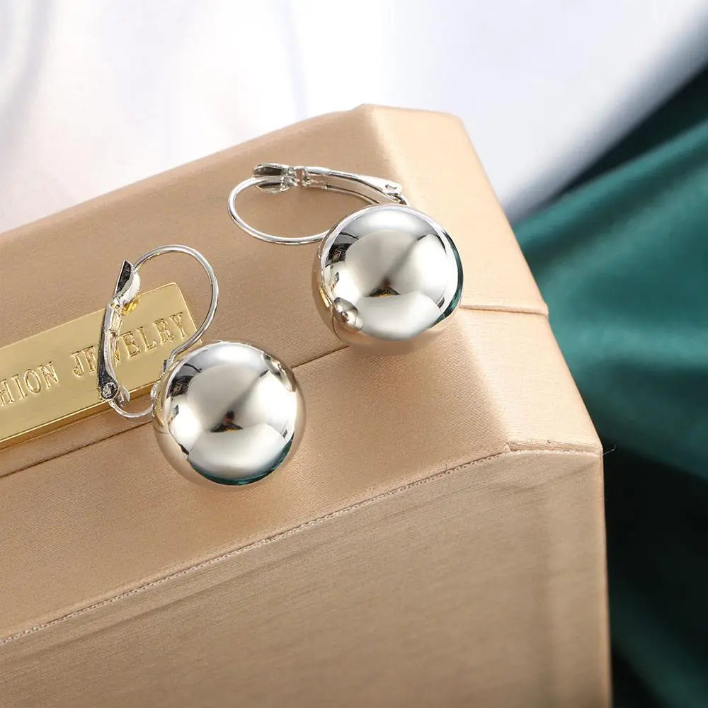 Pendientes colgantes con bola esférica brillante de plata, con cierres de palanca discretos en oro rosa y plata.