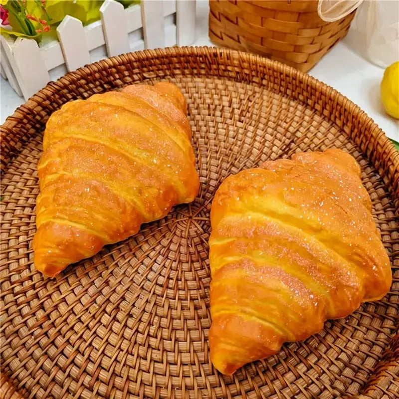 zwei goldbraune, schuppige Croissant-förmige Hundebrot – langsam aufsteigende, weiche Knetspielzeuge mit zuckrigem Zuckerguss, ruhend auf einem geflochtenen Weiden-Tablett