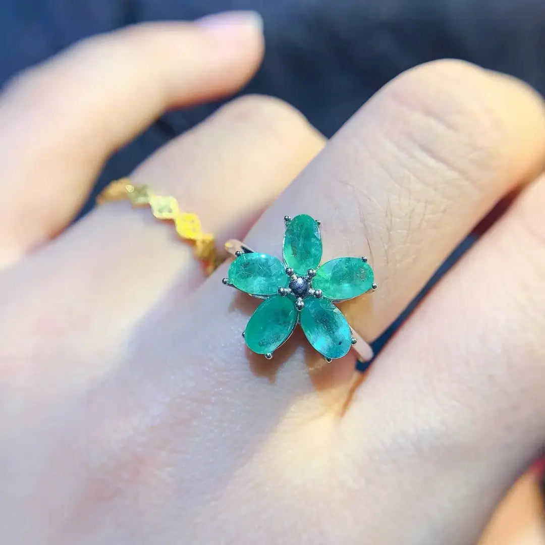 Ein Smaragdblumen-Silberring mit einem kräftigen grünen Fünfblüten-Design aus Smaragdschliff sowie einem dunklen Zentrum, das in einem silberfarben wirkenden Metall eingefasst ist.