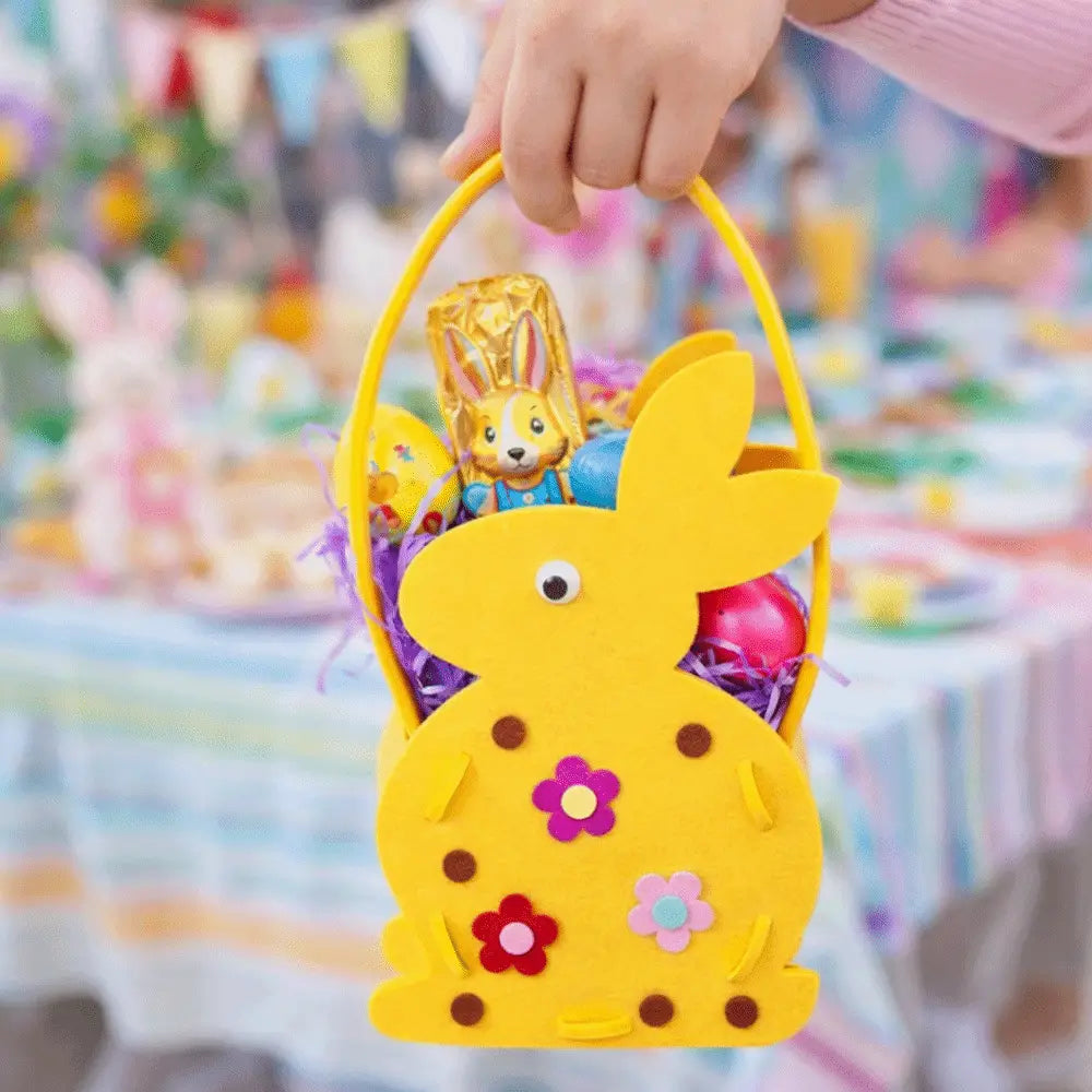 A bright yellow felt easter bunny basket gift bag with embroidered flowers and brown polka dots holding colorful candies and purple shredded paper.