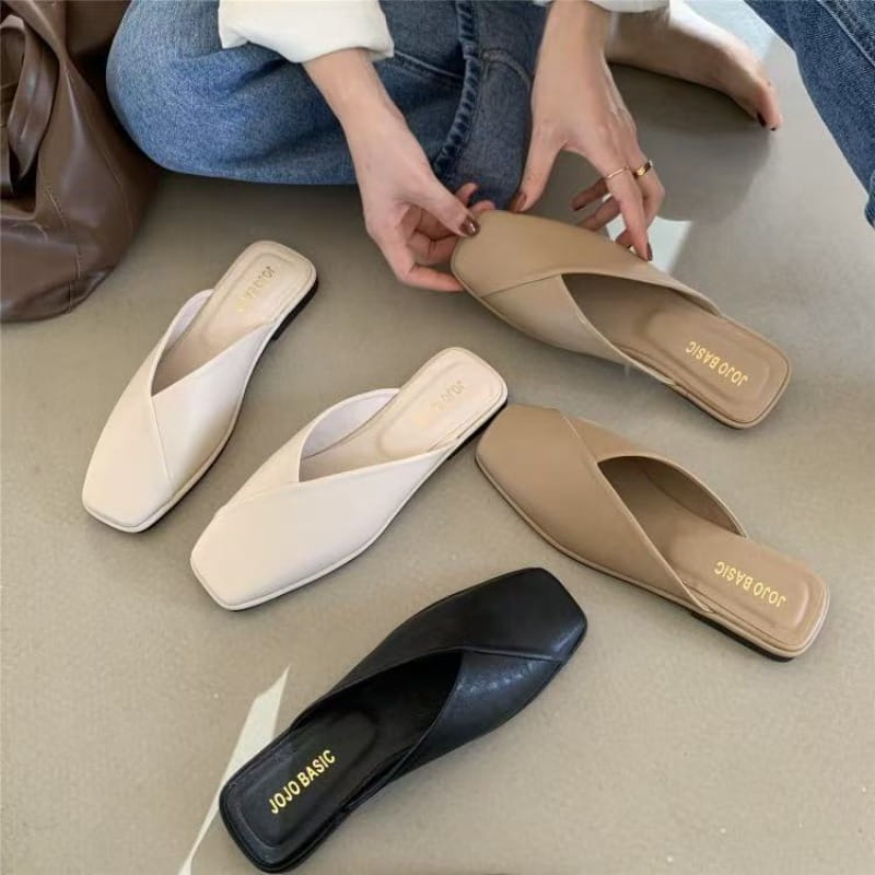 Beige und schwarze flache Ledermules mit einem quadratischen Zehenbereich und weicher, glatter Lederoberfläche.