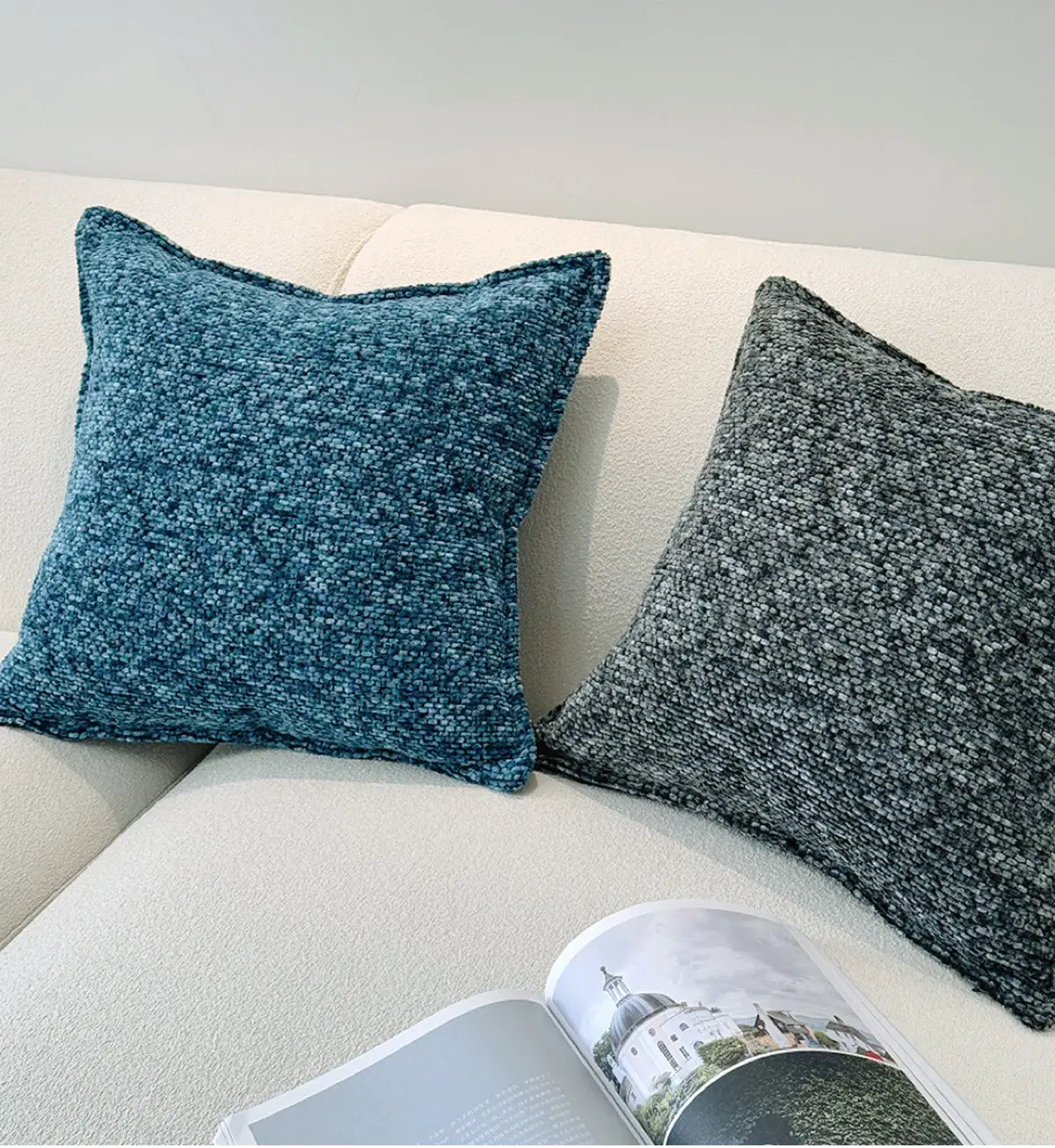 Deux housses de coussin d’appoint en chenille aux tons riches de bleu canard et de gris atténué, avec des éclats blancs, présentent des motifs décoratifs texturés sur un canapé de couleur claire.