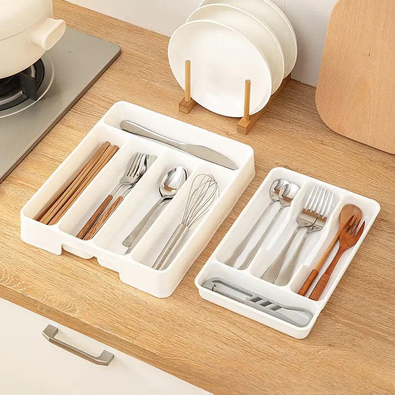 Bac d’organisation réglable pour ustensiles de cuisine en plastique blanc, pour tiroir, avec compartiments segmentés accueillant divers couverts et des cuillères en bois.