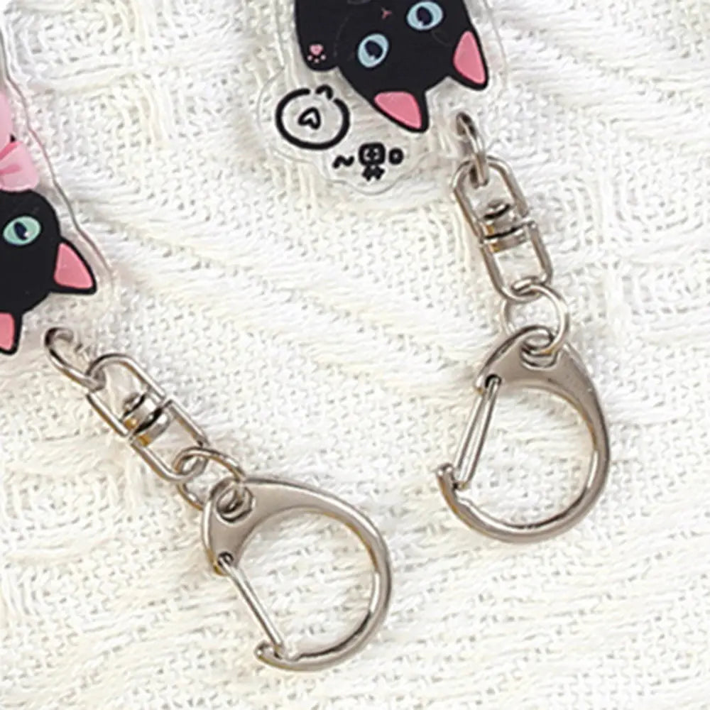 Clear acrylic black cat keychain with pink inner ears and blue eyes attached to silver-toned metal clasps for use as a cartoon animal bag charm.