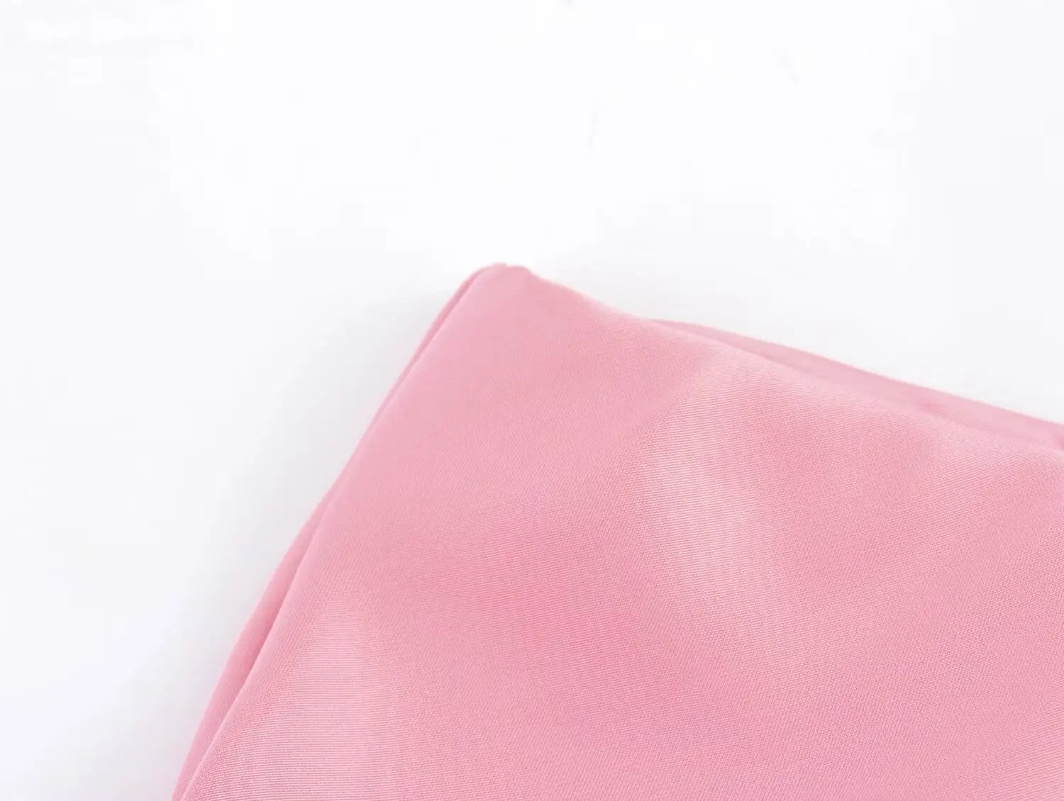 Un carré de poche en satin rose tendre, surface lisse légèrement réfléchissante et bords soigneusement repliés pour une jupe midi en satin à taille haute, élégante.