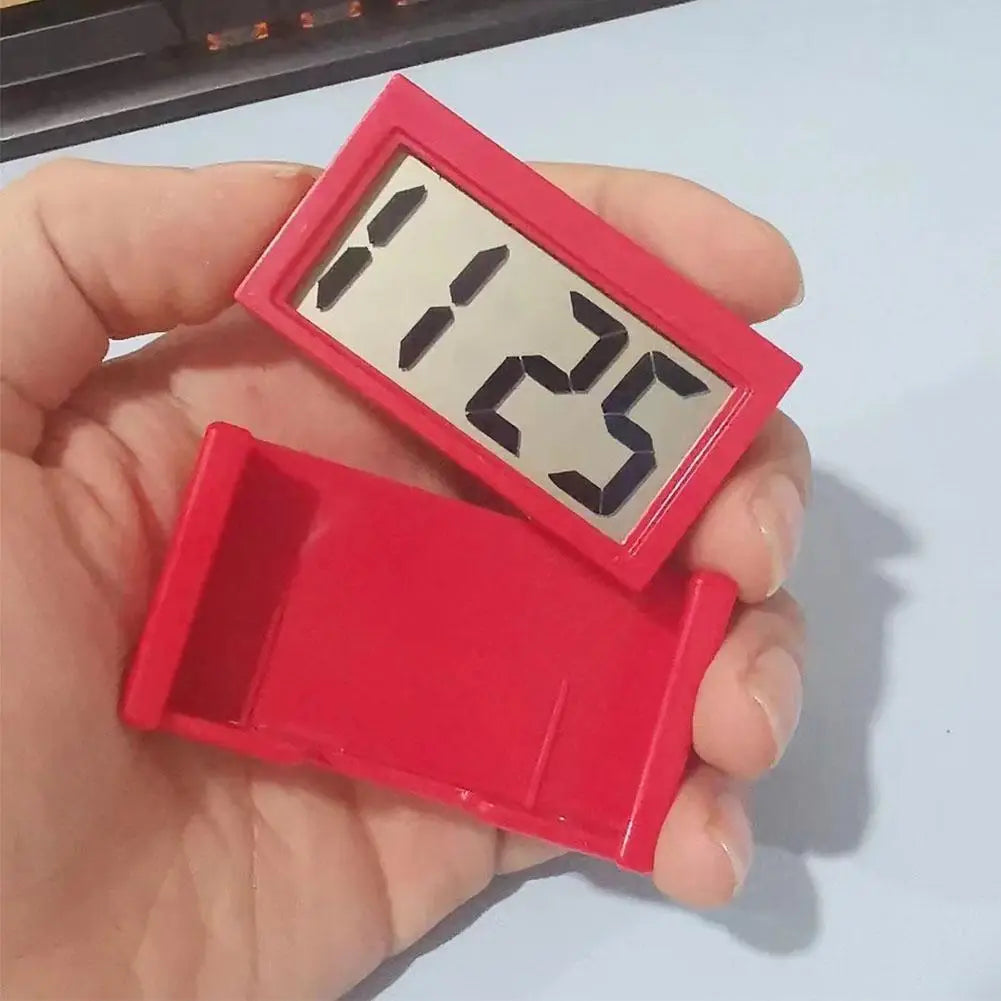 Rote rechteckige digitale Fahrzeuguhr mit schwarzen Ziffern auf einem silbernen Display, das in der Hand gehalten wird, zur Anzeige der Fahrzeituhrzeit im Armaturenbrett.