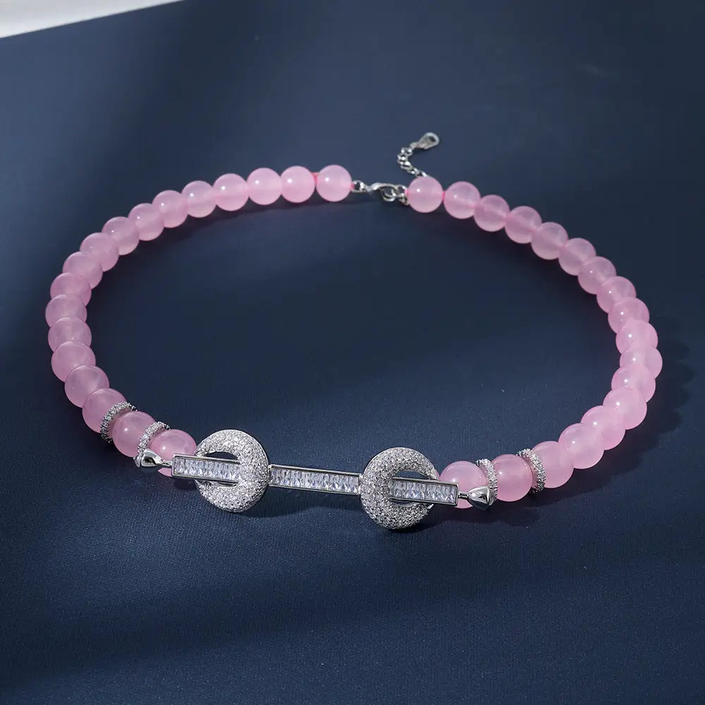 Un delicado collar tipo choker con cuentas de cuarzo rosa en tono rosa, que presenta un broche central de tono plateado adornado con circonita cúbica brillante y detalles circulares.