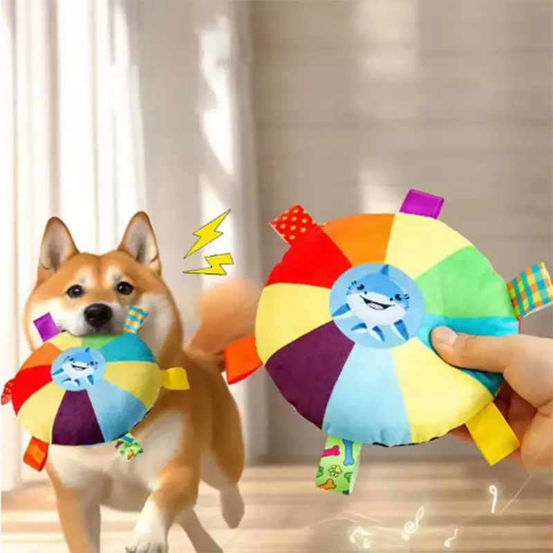 にこやかなサメの顔をあしらい、レインボーの布製つかみタブを備えた、カラフルで丸い犬用のぬいぐるみ玩具。ふわふわした子ども向けの、柔らかく魅力的なおもちゃのタイプです。