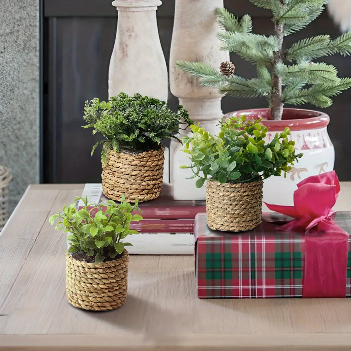 Three small woven wicker planters containing green artificial eucalyptus flowers as small potted plants measuring 17cm.
