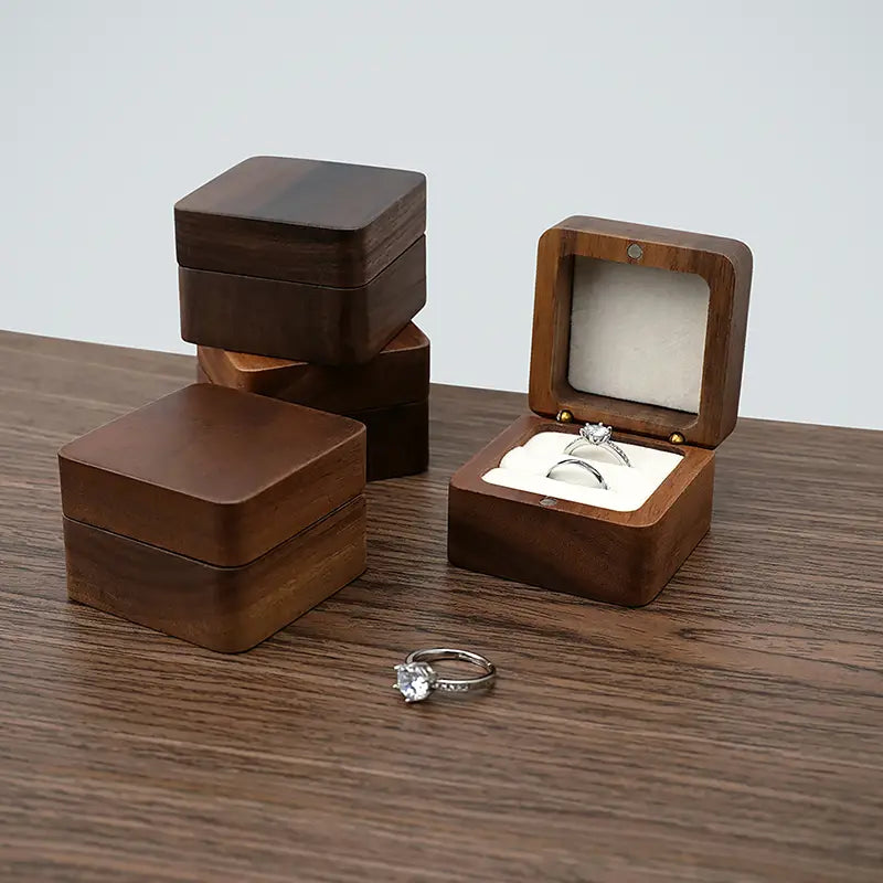 Boîte à bague en bois brun foncé avec couvercle à charnières et intérieur en velours blanc, ouverte pour présenter deux bagues en tant que présentoir d’engagement pour une proposition de mariage.