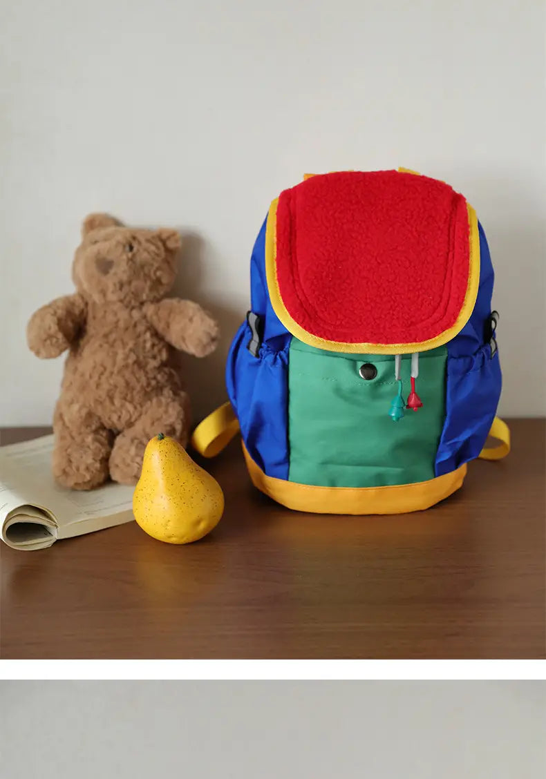 Ein lebhaftes mehrfarbiges leichter Fuzzy-Rucksack für Kinder mit plüschigem rotem Oberteil, blau-grünem Körper und gelber Verzierung, entworfen als Kindergartentagesrucksack.
