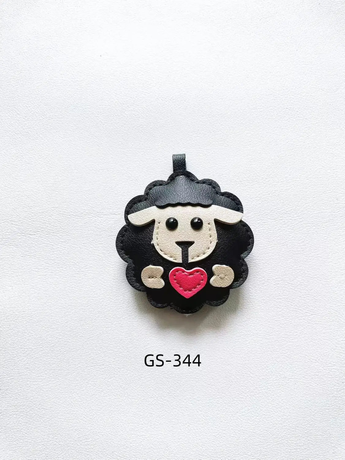 Black leather sheep keychain with white facial features and a red heart held in its paws as a cute animal bag charm.
