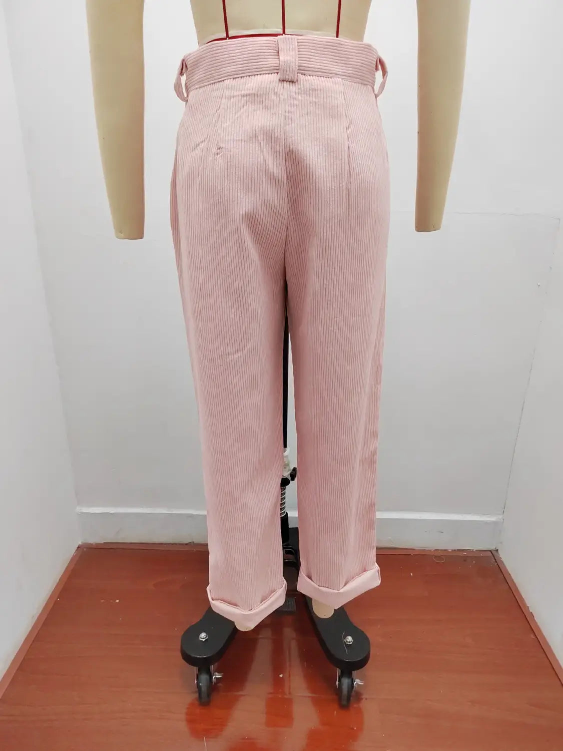 Pantalon en velours côtelé rose à fines rayures, taille haute ample, avec une ceinture assortie et des bas retroussés.