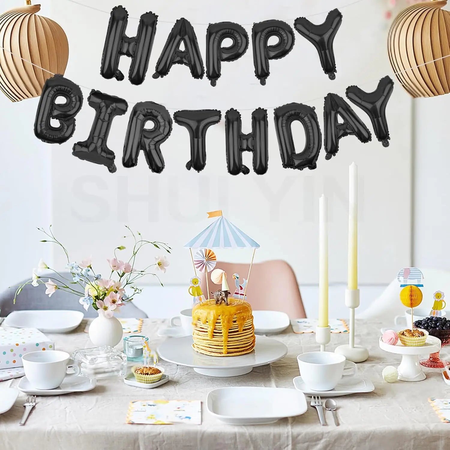 Schwarze Happy-Birthday-Ballon-Banner-Folienbuchstaben im Stil eines aufblasbaren Ballsons, hängend über einem Geburtstagstisch.