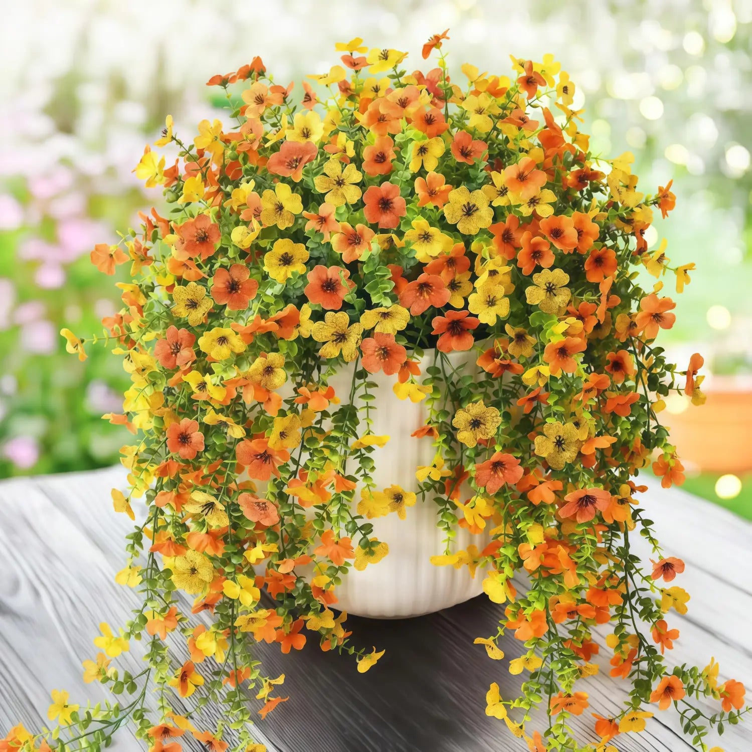 a vibrant cascading artificial flower bouquet featuring orange and yellow morning glory vines with eucalyptus accents in a white ceramic pot