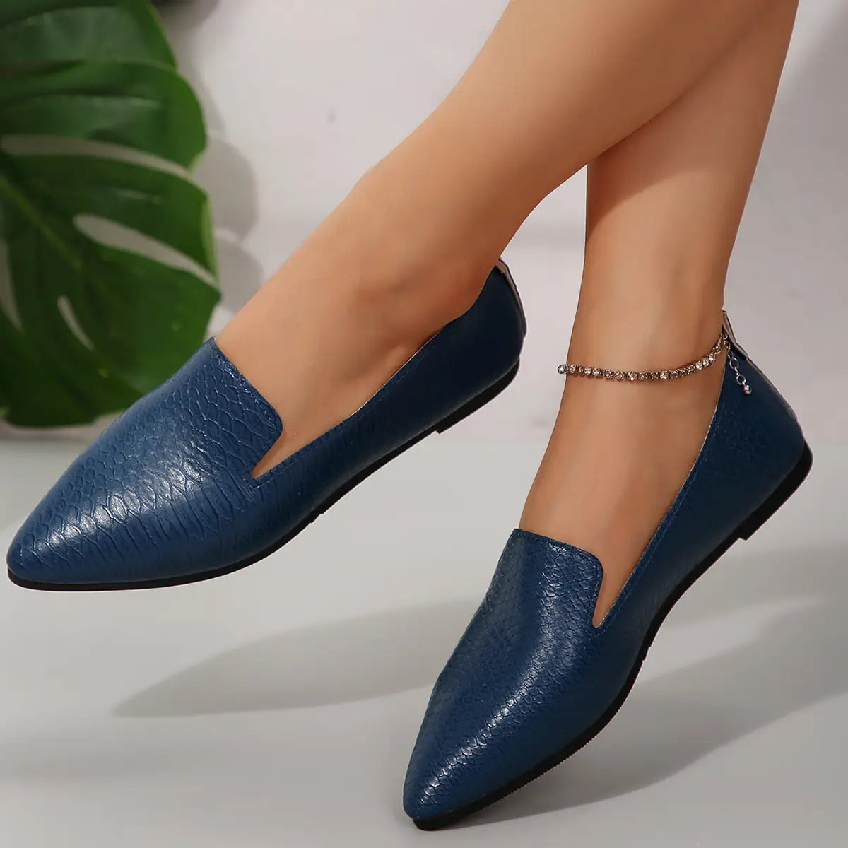Mocasines de cuero con textura de cocodrilo azul, punta afilada, con suela negra, diseñados como mocasines planos para poner y quitar con facilidad.