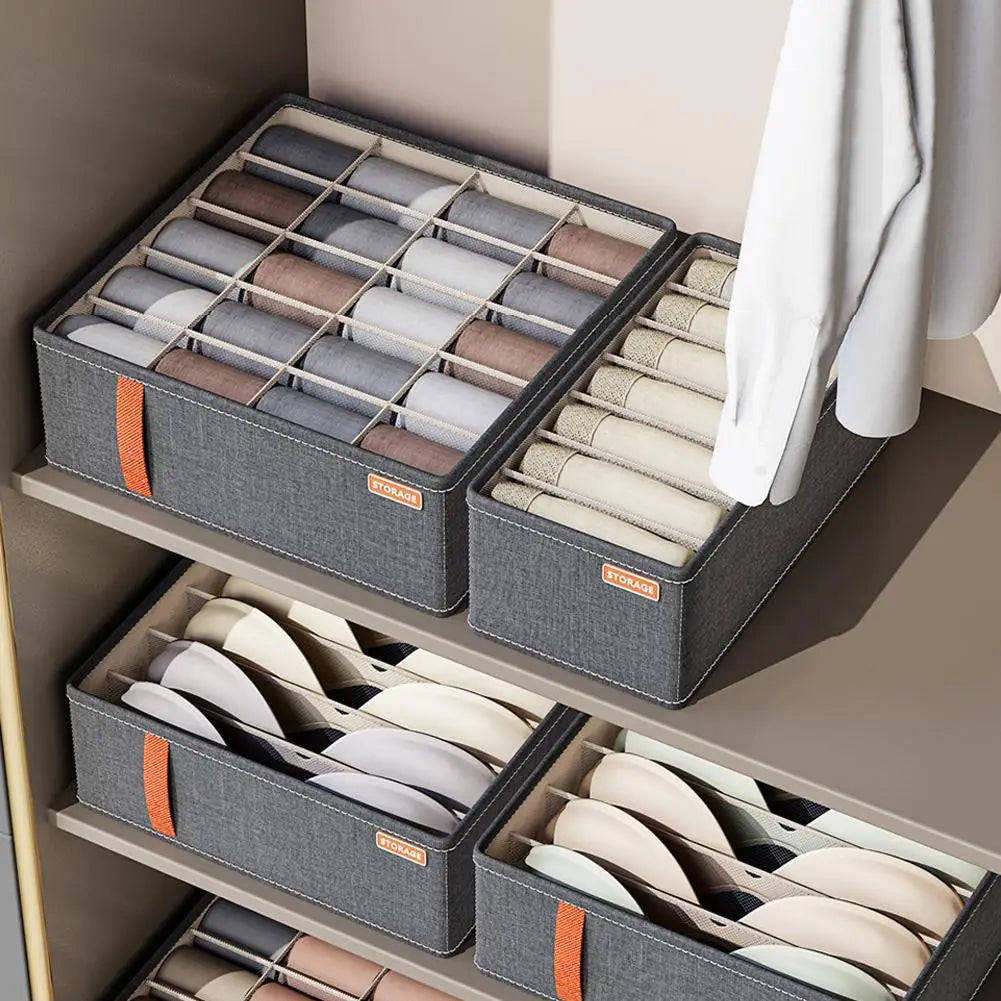 Graue Stoff-Schubladenorganizer-Boxen mit orangefarbenen Riemen und Aufbewahrungsschildern, ausgelegt zur Organisation von Unterwäsche und BHs im Schrank.