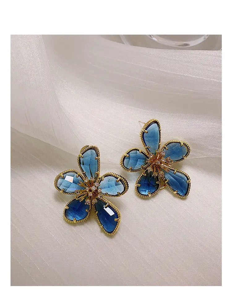 金色調の金属フレームを用いた、青い花形のファセットカットクリスタルの花びらが特徴のエレガントなゴールドフラワークリスタルスタッドピアス。