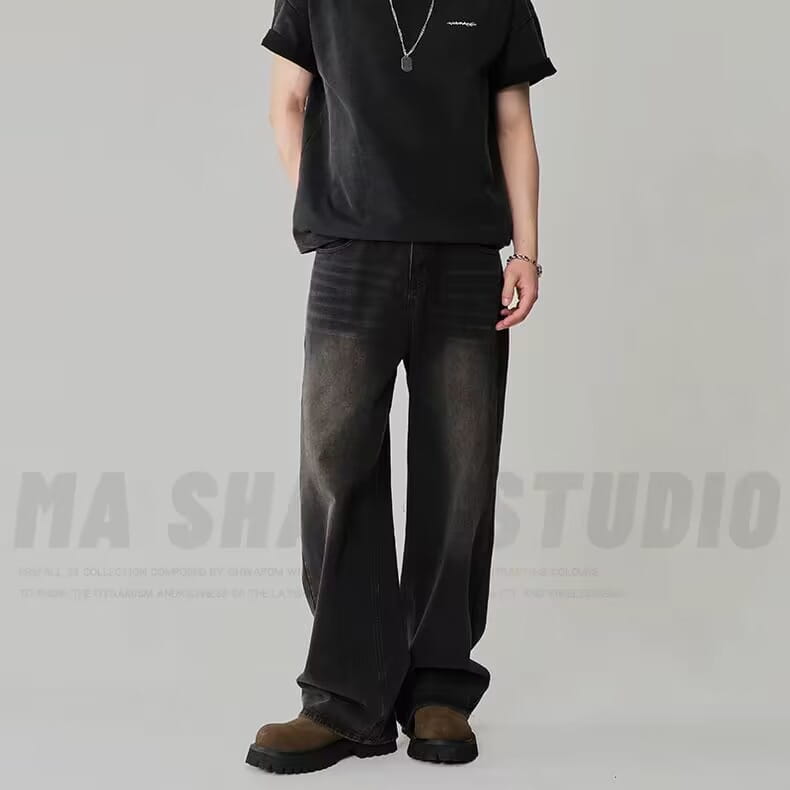 デニム素材で作られた、ブラックのメンズ向けワイドレッグダメージ加工デニムジーンズ。太もも部分に色褪せと控えめなダメージ感が見られる。