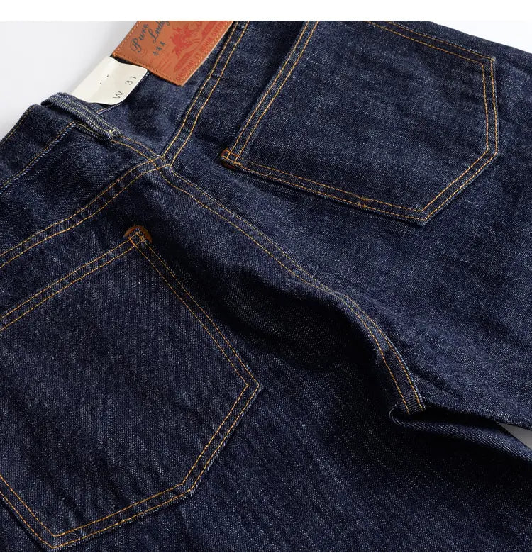 Heavyweight red selvedge denim jeans in dark indigo with contrasting tan stitching and a brown leather brand patch on the waistband showing the back side.