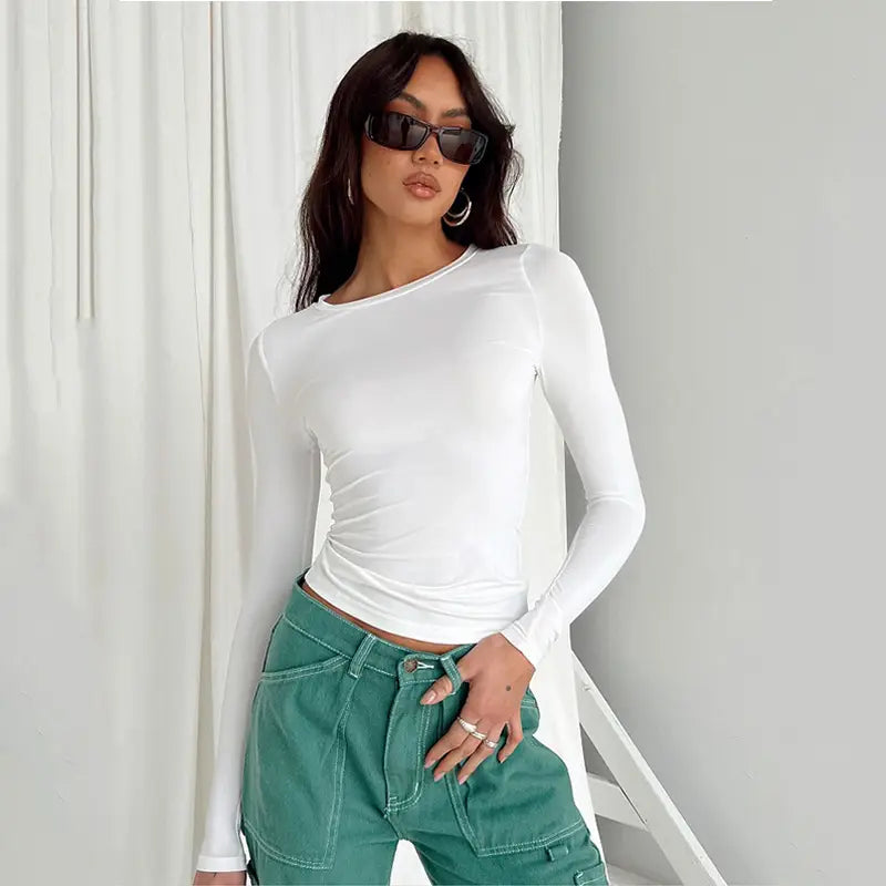 Blusa corta ajustada tipo slim fit blanca para mujer, con mangas largas fruncidas, que presenta una silueta entallada y un detalle fruncido en el lateral.