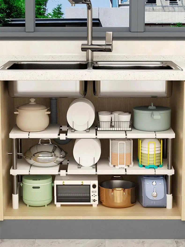 Étagère de séparation à couches réglable blanche avec supports métalliques tenant des assiettes, des bols et des ustensiles de cuisson, conçue comme un support télescopique pour évier afin d’organiser la cuisine