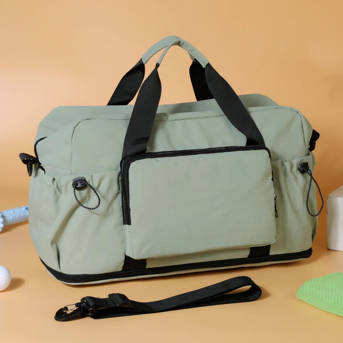 Un sac de voyage duffel léger extensible élégant en vert sauge, avec des poignées et une bordure renforcées noires.