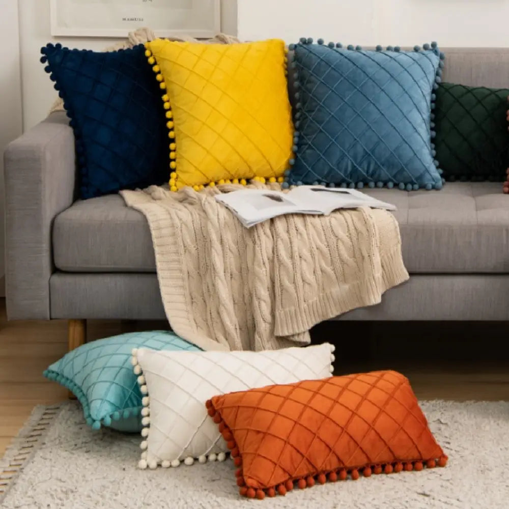 ensemble de housses de coussin en velours colorées bleu marine, jaune, bleu canard, blanc et orange, avec motifs losange matelassés et garniture à pompons, complétant une housse de coussin en velours gris avec pompons recevant des retours positifs.