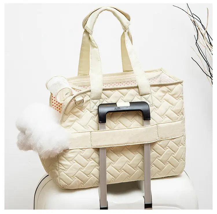 Sac pour animal de compagnie matelassé de couleur crème, avec une poignée rétractable noire et une touche de pompon blanc duveteux, conçu comme un petit porte-chien respirant.