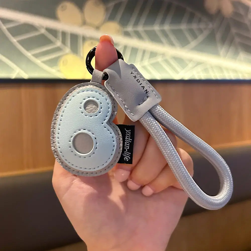 Light blue leather initial keychain shaped like the number eight with silver stitching and a matching braided strap wristband charm.