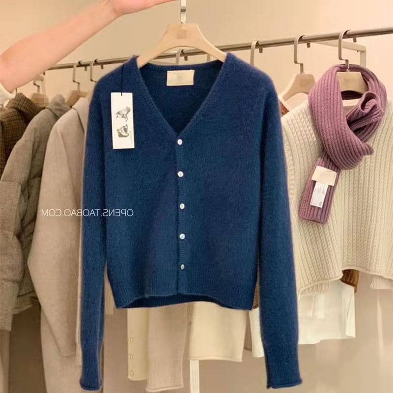 Un pull cardigan en laine mérinos bleu foncé à encolure en V, à manches longues, avec des boutons de couleur claire et une texture tricotée douce.
