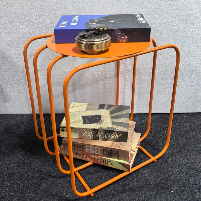Orange metal side table magazine rack with curved frame and two shelves for minimalist storage.