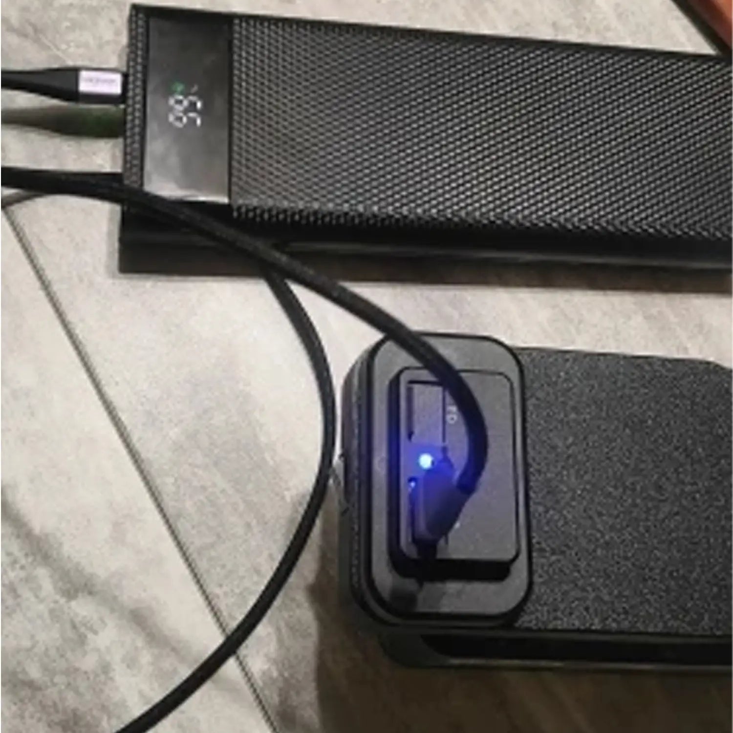 Black textured ferrex 20v power bank with digital display showing 87 percent charge and blue led light indicating fast charging via usb adapter.