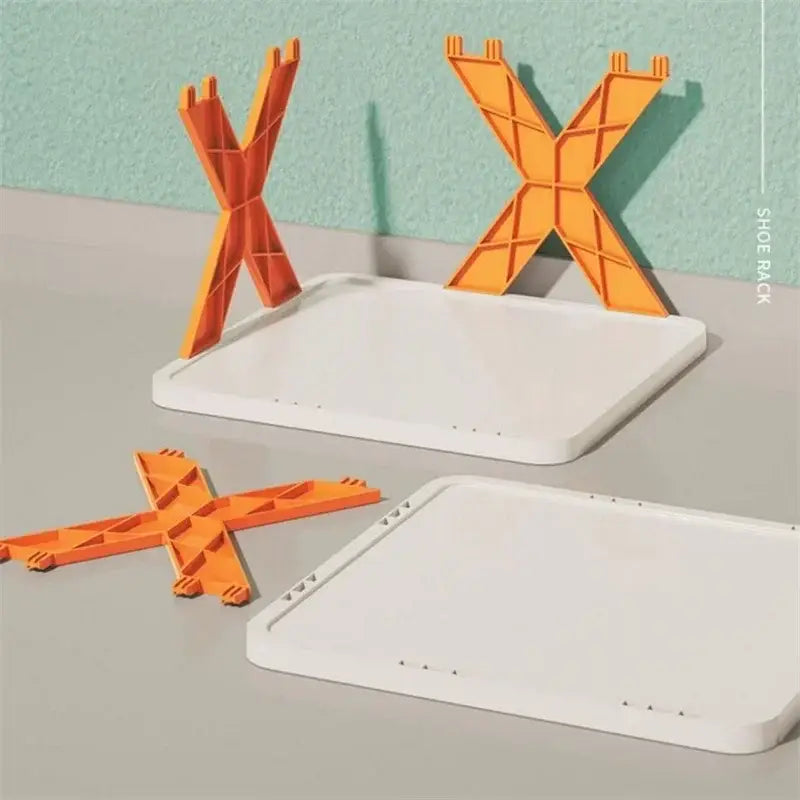 El soporte para zapatos plegable y apilable de plástico naranja con forma de X se sostiene sobre una base blanca rectangular como organizador de estantes para zapatos.