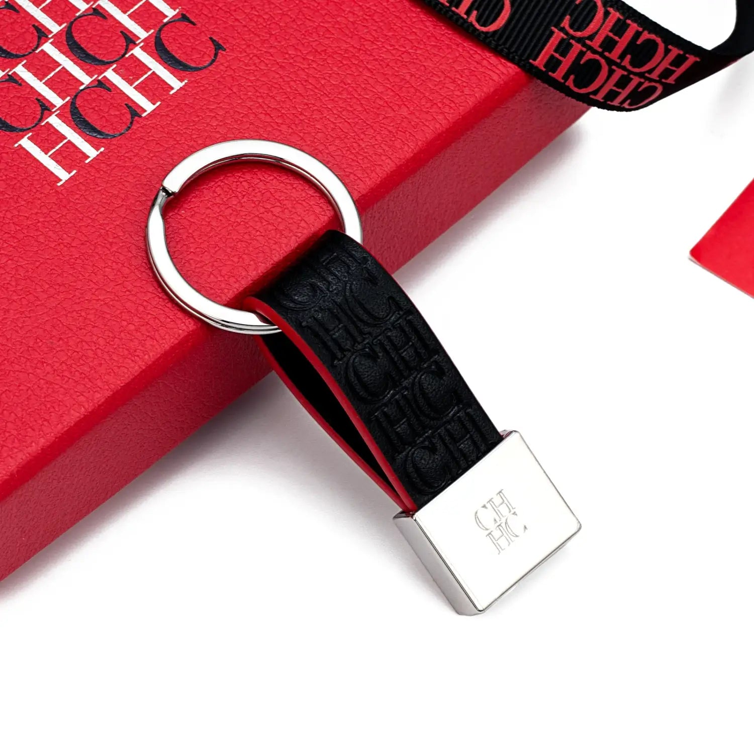 Porta llaves de accesorio de equipaje minimalista de cuero negro con anillo metálico de tono plateado y logotipo ch en relieve sobre una placa rectangular.